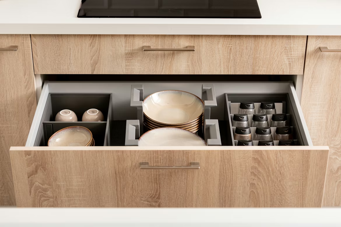 An open kitchen drawer with a gray organizer holding stacked plates, bowls, and small canisters.
